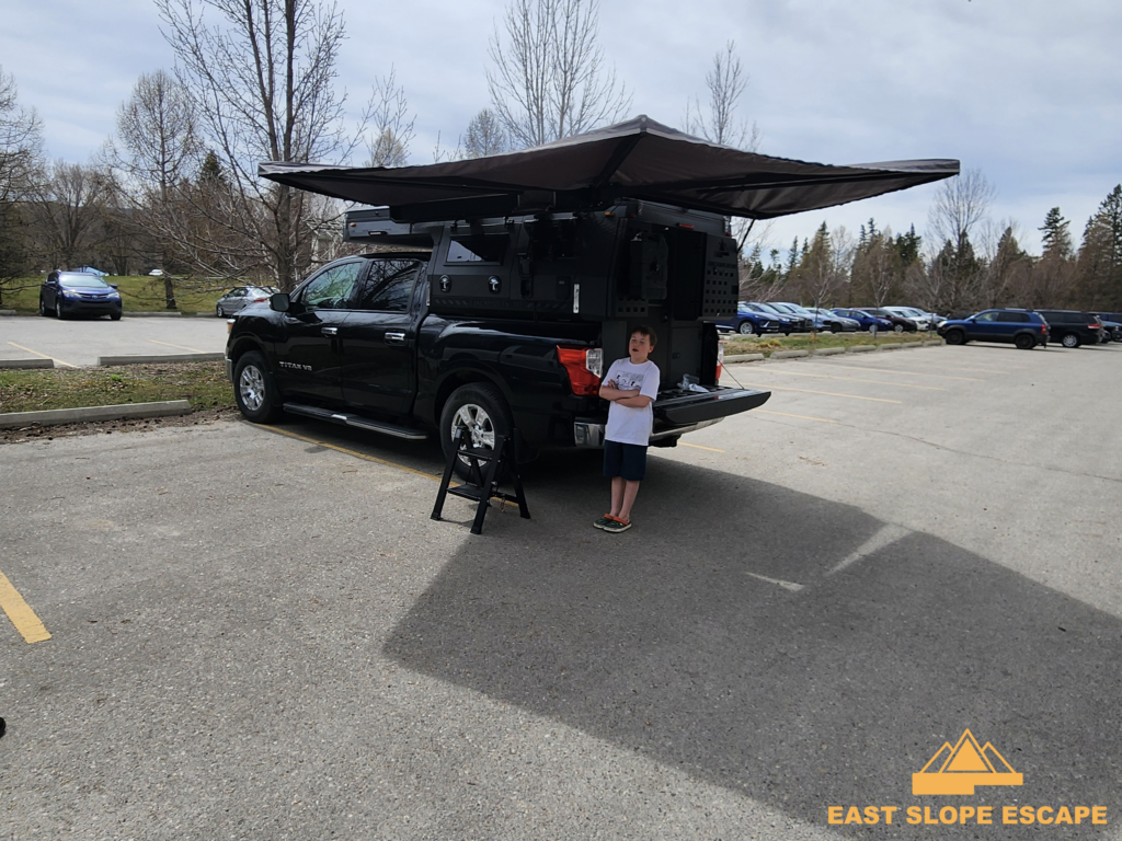 A little boy stands outside of a camper.